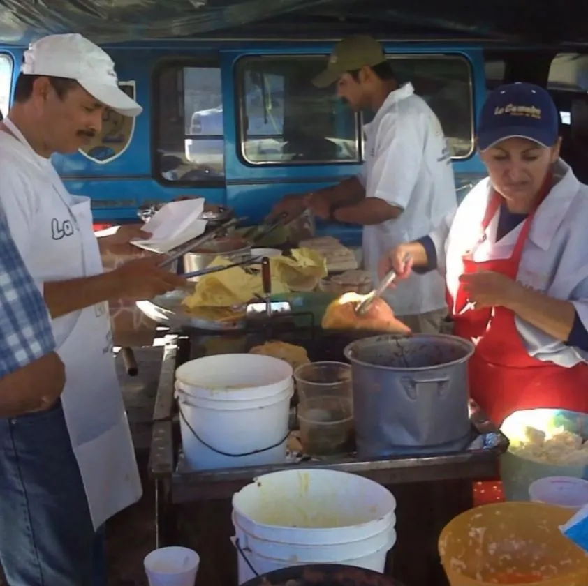 El equipo de La Comadre con gorras y camisas blancas preparando tacos en la plancha