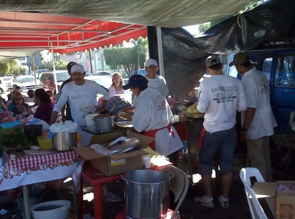 El puesto de La Comadre bajo un toldo rojo, con el equipo de camisas blancas atendiendo a los clientes