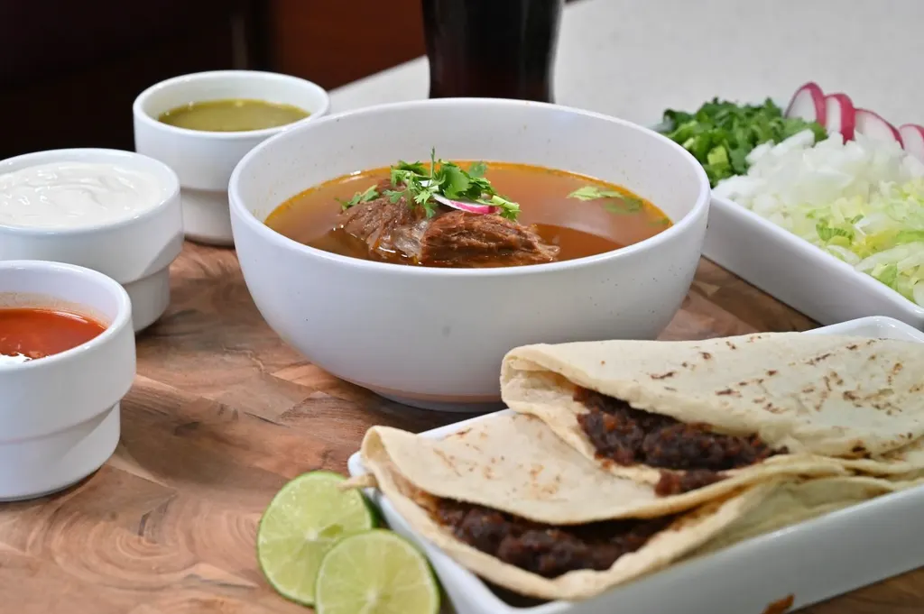 Orden de birria: plato de carne en su jugo con cilantro, salsas, crema y tacos de asiento