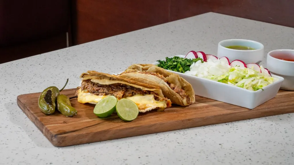 Dos tacos especiales de birria con queso, limones, chiles toreados y verdura picada