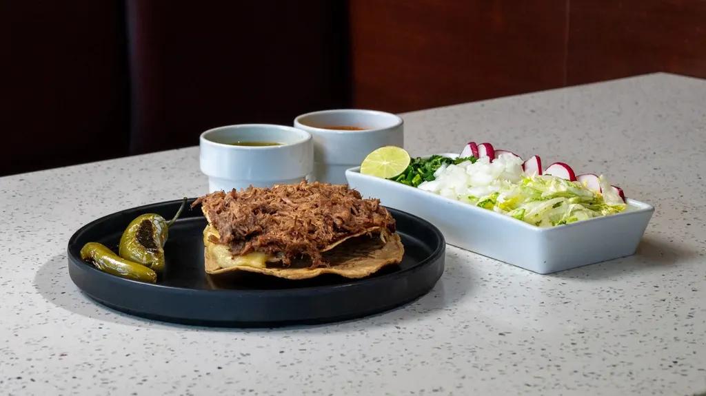 Tostada Cleopatra de birria con queso, chiles toreados, salsas y verdura