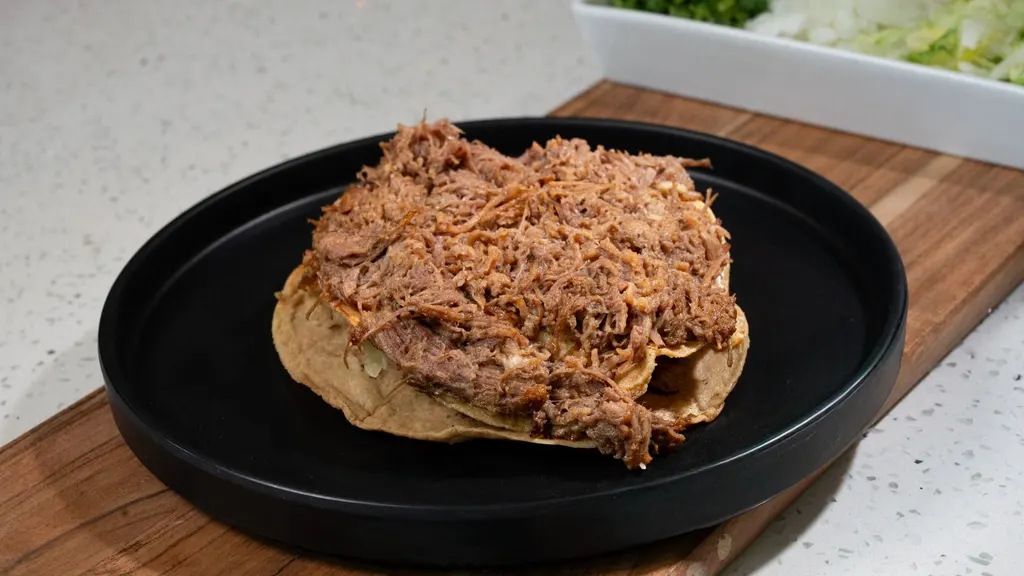 Tostada Cleopatra con birria deshebrada en plato negro